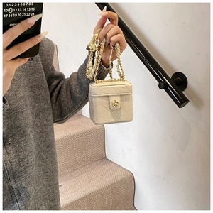 Detailed view of beige mini quilted box bag with gold chain and flower lock clasp