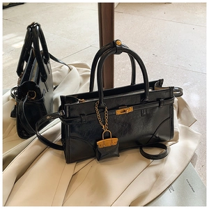 Detail of black textured handbag with golden lock, mini charm and mirror reflection