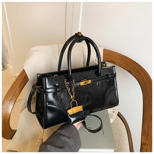 Close-up of black glossy briefcase with gold twist-lock and chain charm on a chair