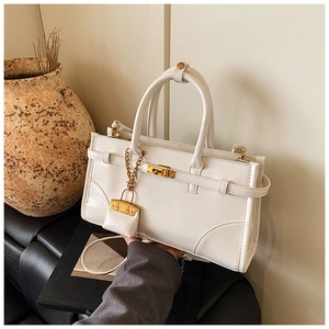 Detail of white leather handbag featuring metal twist lock and decorative belt strap