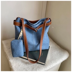 Detail view of denim tote bag featuring brown leather straps and matching small pouch charm