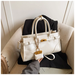 Detail view of white leather handbag with gold buckle and mini charm on beige sofa