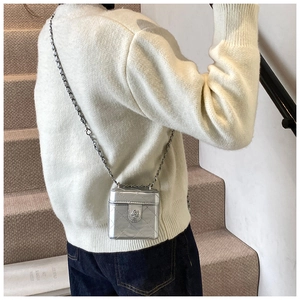 Detail view of mini silver quilted chain bag with camellia hardware on white sweater