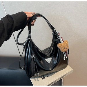 Detail der schwarzen glänzenden Hobo-Tasche mit Bärenanhänger und Metallschnalle