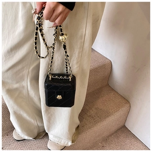 Close-up of black quilted box bag with metal flower clasp and leather woven chain