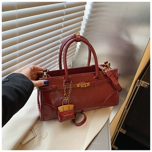 Detail of burgundy glossy leather handbag with golden lock and mini charm accessory