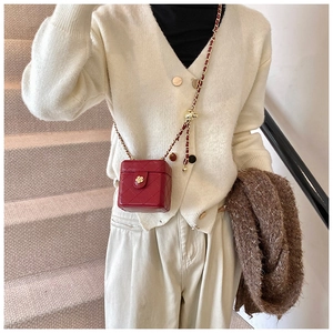 Detail view of red quilted mini crossbody bag with gold chain and flower clasp on a model