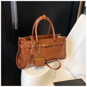 Detail of glossy brown leather tote with metallic lock and mini charm pendant