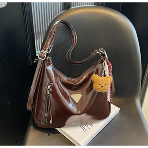 Detail der dunkelbraunen Lackleder-Tasche mit Plüschbär-Anhänger und Metallapplikation