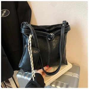 Detail of a black faux leather tote bag with white contrast stitching and a small pouch