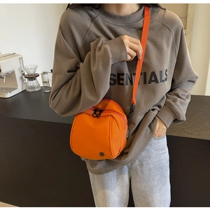 Dettaglio di una borsa a tracolla in nylon arancione brillante con doppie cerniere nere