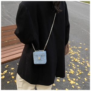 Close-up of a mini denim box bag with gold floral hardware and woven chain strap