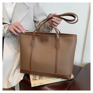 Detalle de bolso tote marrón en cuero granulado con bordes a contraste y logo grabado