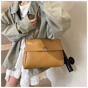 Close-up of caramel faux leather satchel bag with silver square lock on green jacket