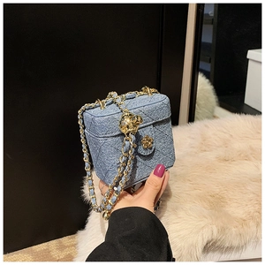 Detail of blue denim quilted mini box bag with golden chain and ball closure