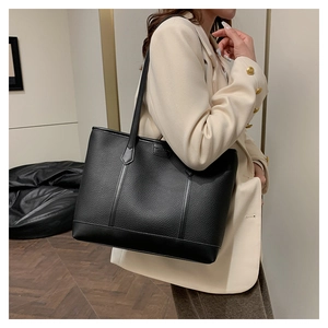 Detalle de bolso tote negro en piel granulada con logo y textura de cuero de calidad