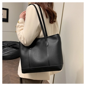 Detalle del bolso tote negro en cuero de grano lichi con una etiqueta rectangular de moda