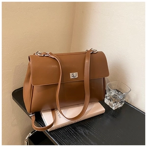 Detail of a brown leather shoulder bag with silver metal swivel lock on a wooden desk