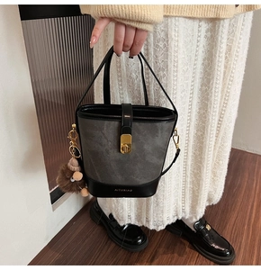 Detail of grey contrast bucket bag with gold clasp and brown plush animal charm