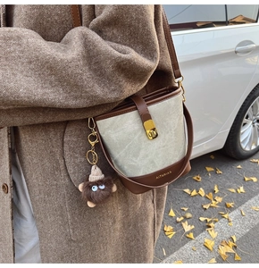 Detail of color-block bucket bag with gold buckle and plush charm on autumn coat