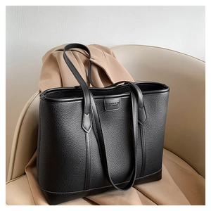 Detalle de bolso tote de cuero granulado negro con parche grabado sobre un asiento