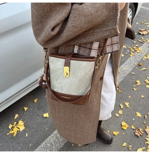 Detail view of canvas bucket bag with brown leather trim and golden logo clasp