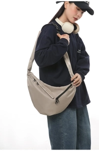 Detail of minimalist beige nylon crossbody crescent bag with front zipper pocket and wide strap