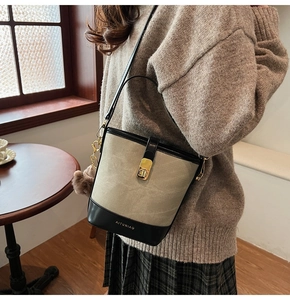 Detail of canvas bucket bag with black leather trim and gold hardware on a model