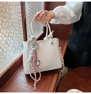Detail of white leather bucket bag with knotted handle and colorful woven rope charm