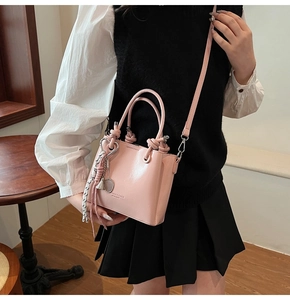 Close-up of pink leather bucket bag featuring unique knot handle and adjustable shoulder strap