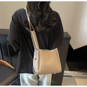 Detail view of the beige lychee texture leather bucket bag with metallic bottom feet