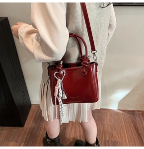 Detail of burgundy glossy bucket bag with golden hardware and heart charm decoration