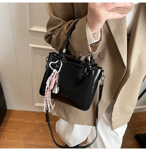 Detail of black glossy bucket bag with heart metal buckle and colorful woven tassel