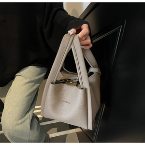 Detail of greyish-brown lychee grain leather handbag featuring embossed brand logo detail