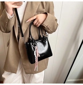 Detail of a black glossy bucket bag with metal handle and woven charm accessory