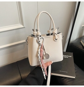 Detail of cream white bucket bag with metal knot handle and creative shuttlecock charm