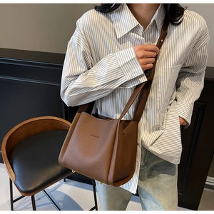 Detail of dark brown pebble leather bucket bag featuring adjustable strap and logo