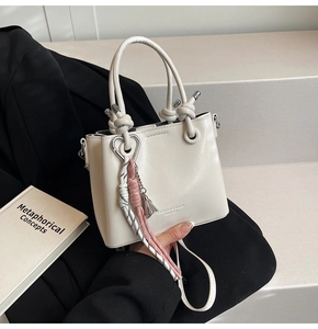 Detail of cream bucket bag with knot handle, heart charm, and tassel on black blazer