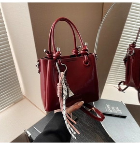 Detailed close-up of dark red oil wax leather bucket bag with decorative woven pendant