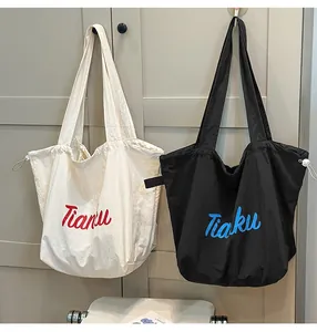 Detail view of large capacity nylon tote bag with drawstring sides and embroidered lettering