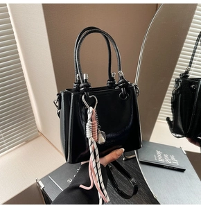 Detail of black glossy bucket bag with woven rope charm and detachable strap