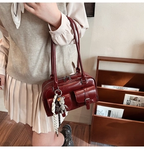 Detailed side view of deep red retro Boston bag with functional pockets and bear charm
