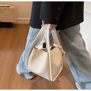 Detail view of cream lychee texture leather handbag with brand logo and soft bucket shape