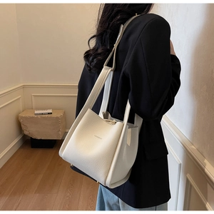 Close-up of cream lychee-grain leather bucket bag with brand logo and shoulder strap
