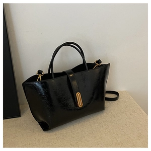 Detail of black oil wax leather bucket bag featuring a gold oval clasp and glossy texture