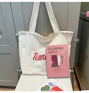 Close-up of beige nylon tote bag featuring red embroidered letters and long shoulder straps