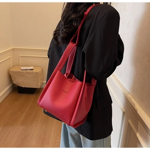 Detail of lychee textured leather bucket bag with black brand lettering in deep red