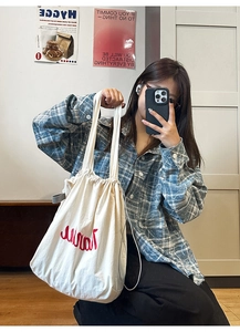 Close-up of cream white drawstring tote bag with red embroidery in a cozy home setting