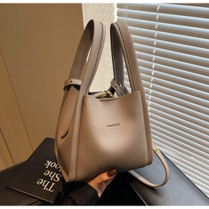 Detailed macro view of litchi pattern leather texture and gold hardware on grey bucket bag