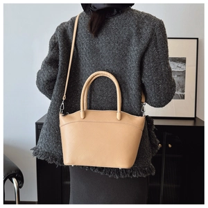 Close-up of khaki bucket bag with geometric stitching on a textured tweed background